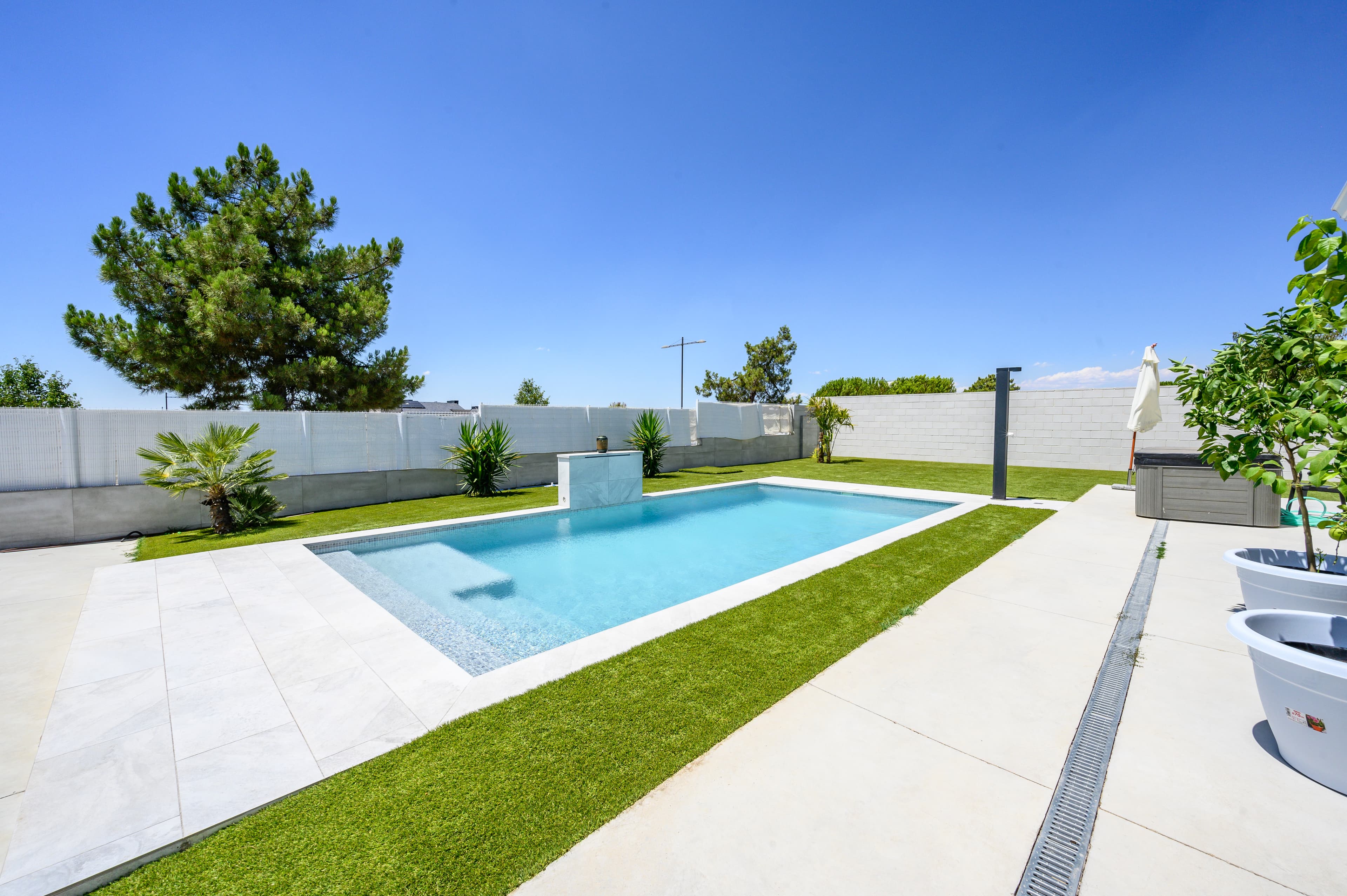 Piscina rectangular con césped y losas de gran formato en jardín vallado